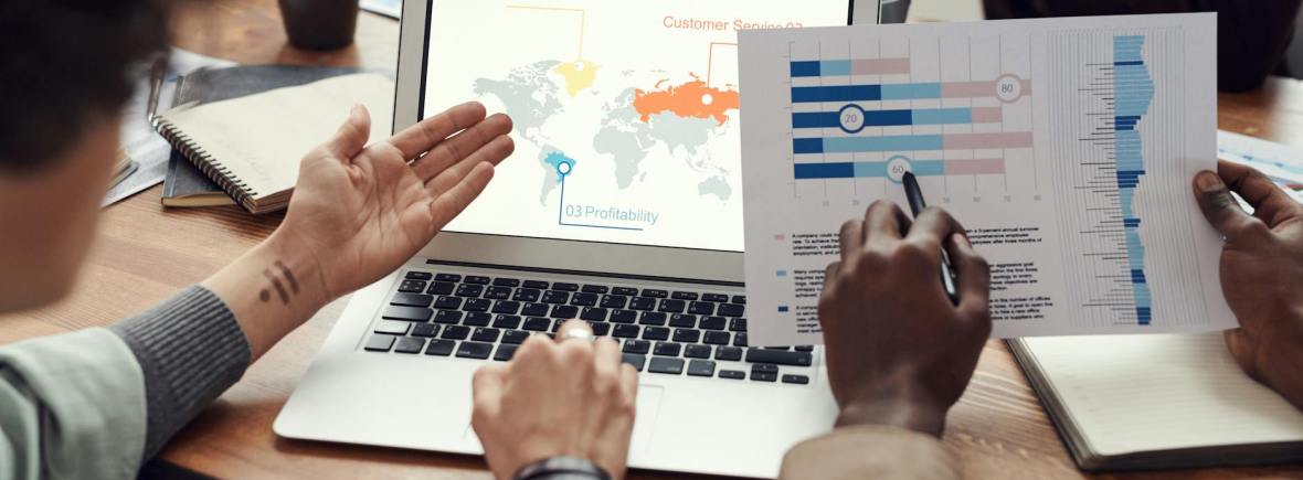 Dr. Tekin Köse - Akademik Mentor ve Ekonomist, Brighton Üniversitesi The image shows two people working together on a laptop, reviewing financial data and visualizations displayed on the screen. The laptop is placed on a desk, and the individuals are using their hands to interact with the data. A world map and various charts and graphs can be seen on the laptop screen, indicating they are engaged in data analysis and business reporting.